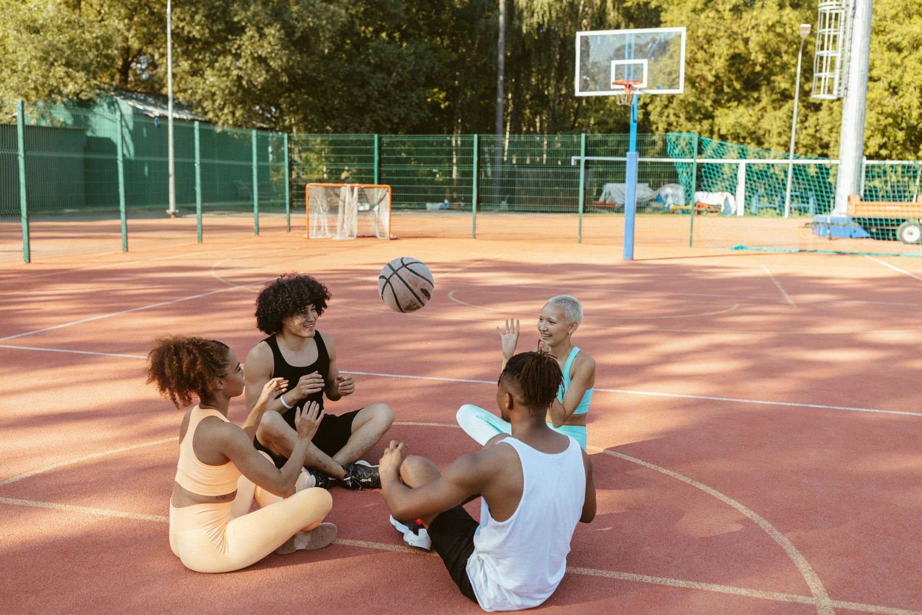 Group of friends having fun playing with a basketball on an outdoor court during the day.